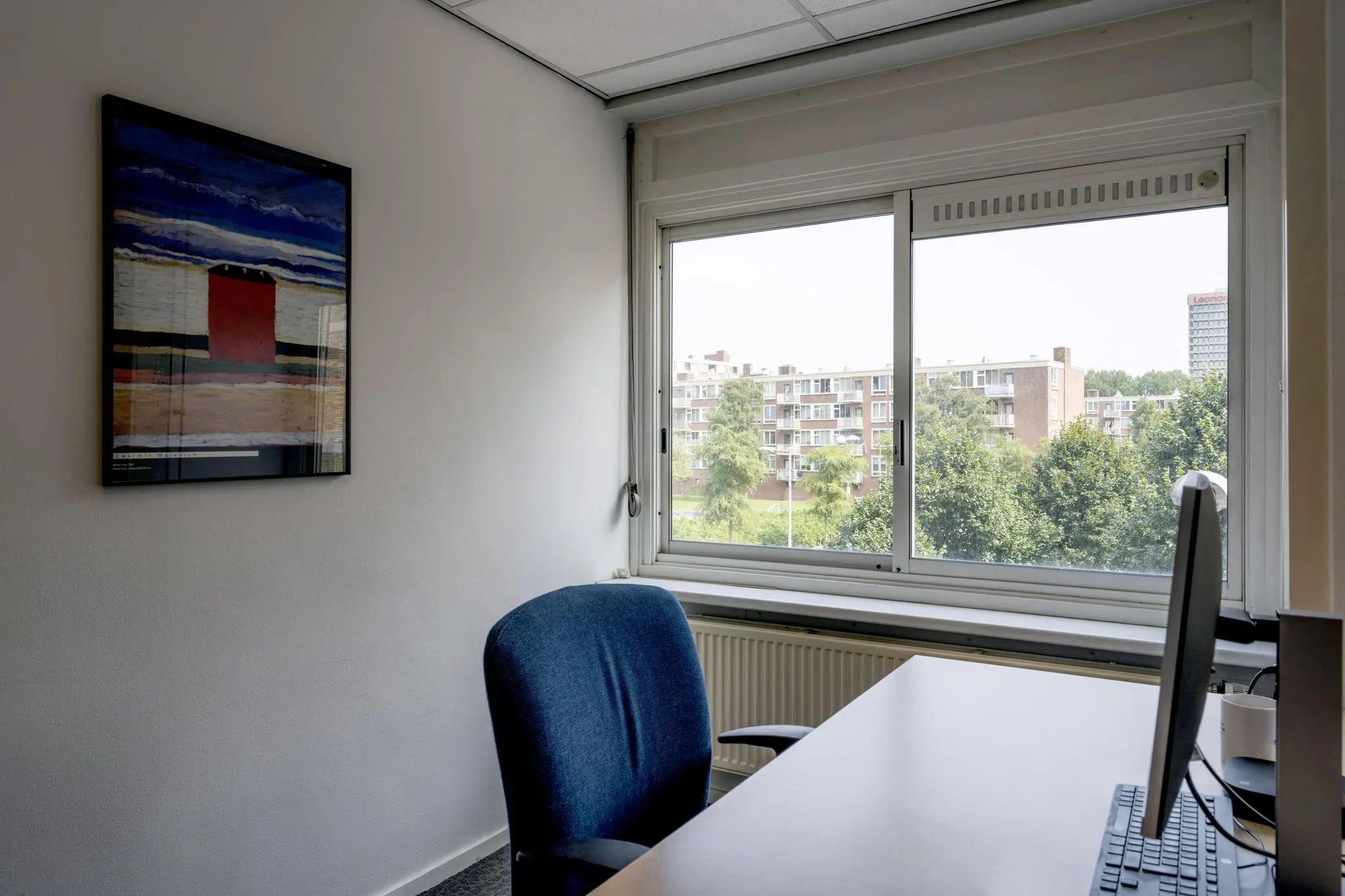 Kantoorruimte aan de Jan Tooropstraat met bureau, bureaustoel, computerscherm en een raam met uitzicht op een woonwijk.